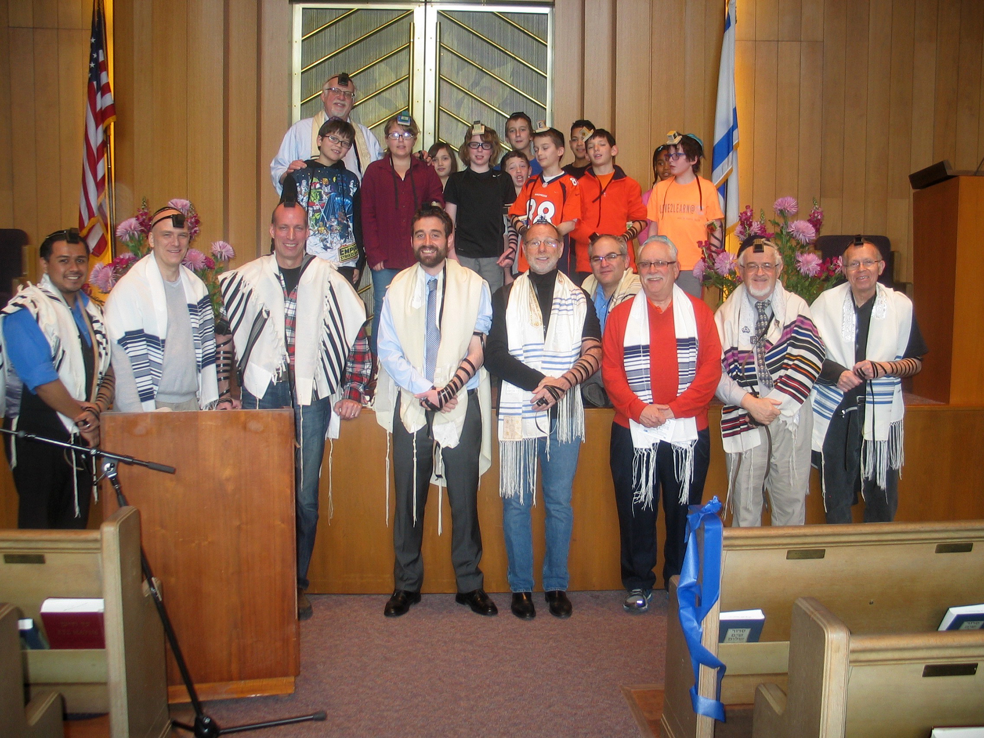 Members of the Men's Club at Temple Har Zion in Illinois along with young members standing on the stage behind them.