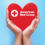 Two hands holding a red paper heart that has the American Red Cross Logo on it.