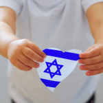 A child holding a heart-shaped cutout of the Israel flag